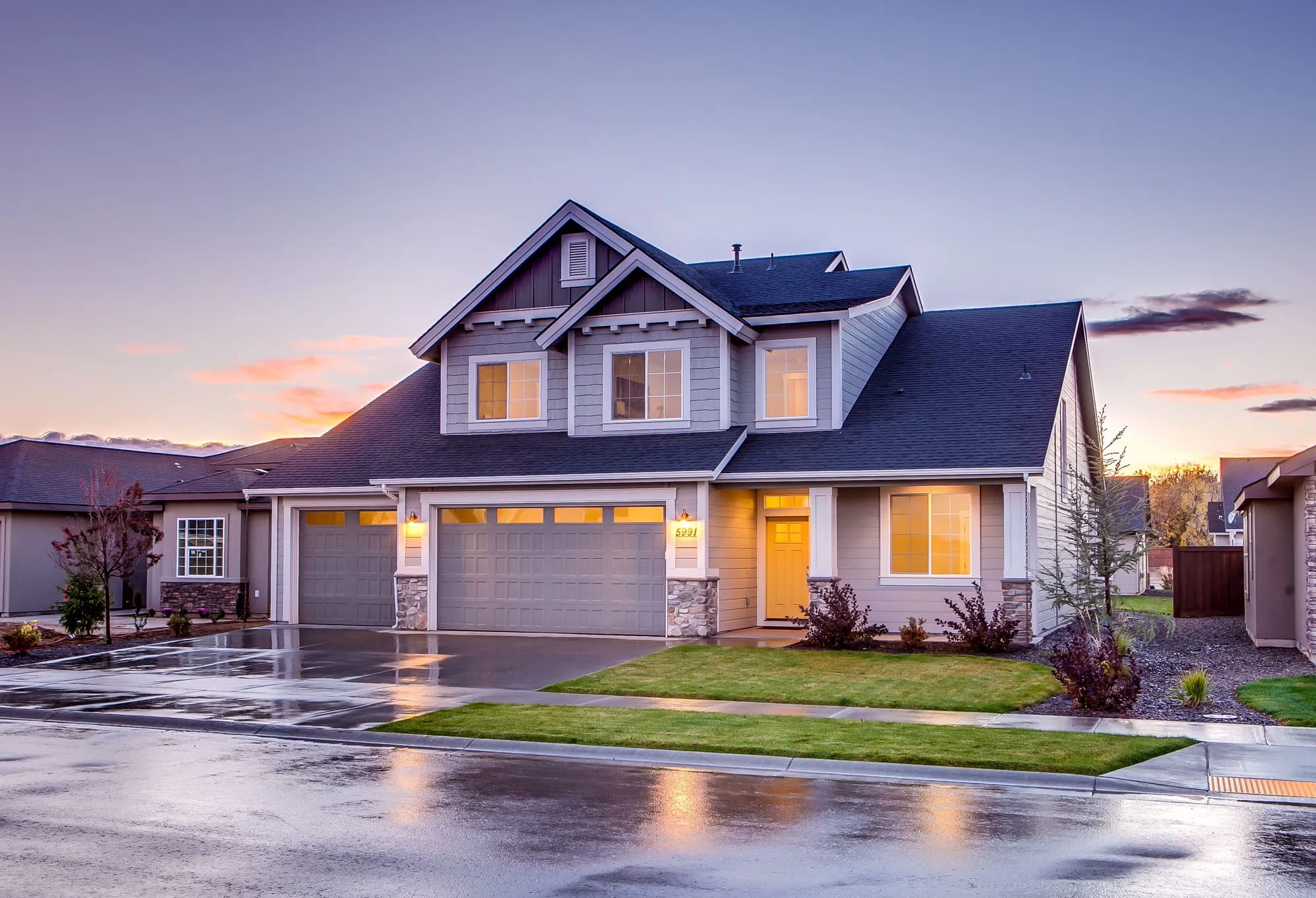 A craftsman-style home at dusk with warmly lit windows and a three-car garage